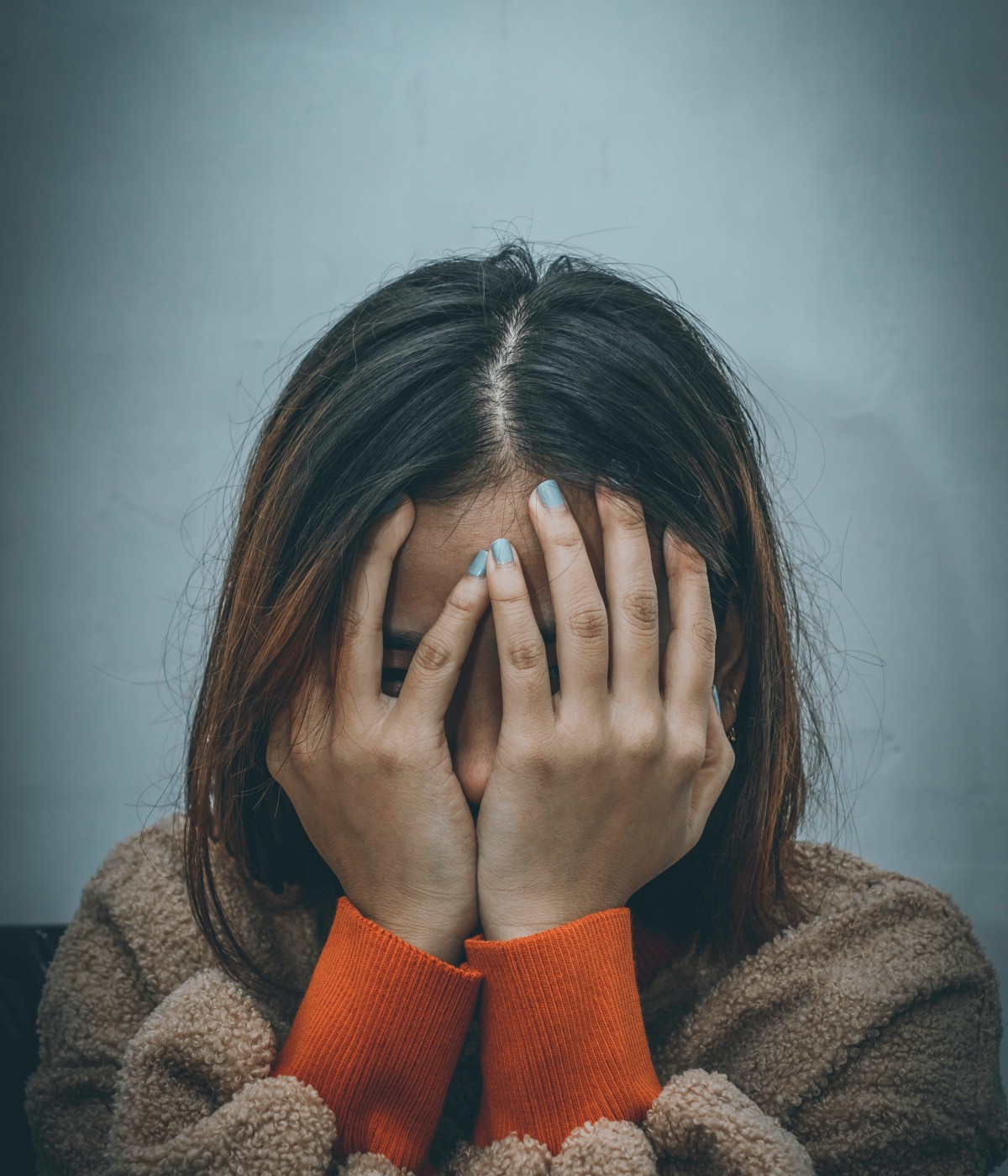 Traurige Person hebt die Hände vor das Gesicht